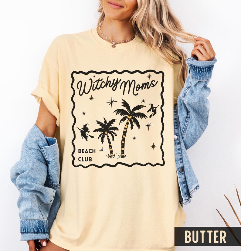 K&ouml;nnte beinhalten: Hellgelbes T-Shirt mit schwarzem Aufdruck &bdquo;Witchy Moms Beach Club&ldquo;. Das Design zeigt Palmen, Sterne und Hexensilhouetten. Das T-Shirt hat kurze &Auml;rmel und eine lockere Passform.