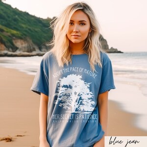 May include: A blue t-shirt with a white graphic of a tree and the text "Adopt the pace of nature. Her secret is patience. Ralph Waldo Emerson."