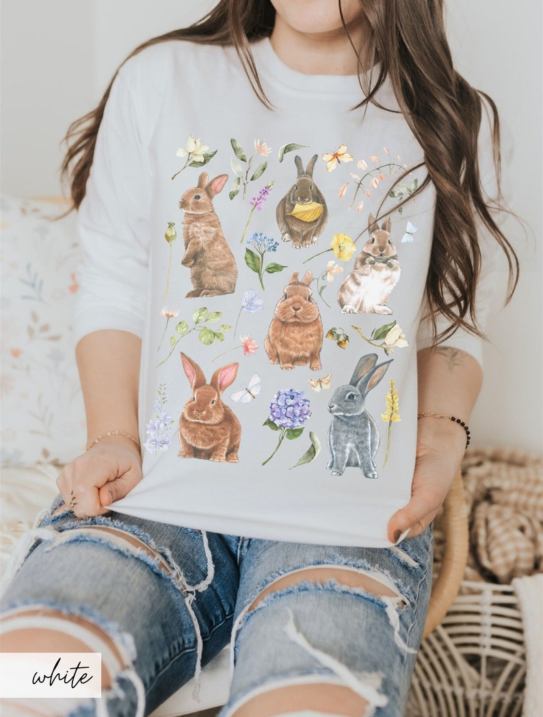 May include: White sweatshirt with a colorful floral pattern and multiple brown and gray rabbits. The rabbits are surrounded by flowers, leaves, and butterflies.