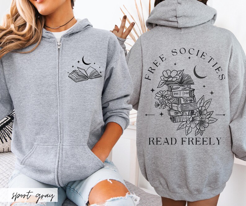 May include: A light gray zip-up hoodie with a black graphic of an open book, moon, and stars on the front. The back features the text "FREE SOCIETIES READ FREELY" with a stack of books, flowers, and a crescent moon.