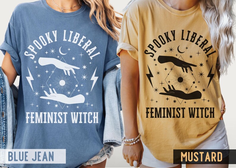 Puede incluir: Dos camisetas, una azul vaquero y otra mostaza, con el texto "Spooky Liberal Feminist Witch". El dise&ntilde;o incluye manos, rayos, estrellas y una luna creciente. Las camisetas son ropa casual.