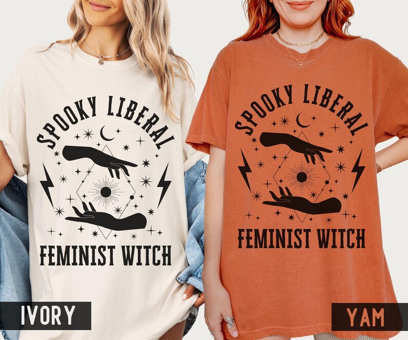 Puede incluir: Camisetas de color marfil y &ntilde;ame con el texto "Spooky Liberal Feminist Witch" en negro. El dise&ntilde;o incluye manos, una luna creciente, estrellas y rayos. Las camisetas son de manga corta y tienen un corte holgado.