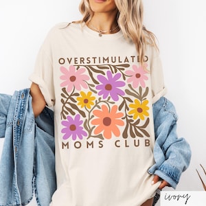 May include: A white t-shirt with a floral design and the text "Overstimulated Moms Club" in brown letters.