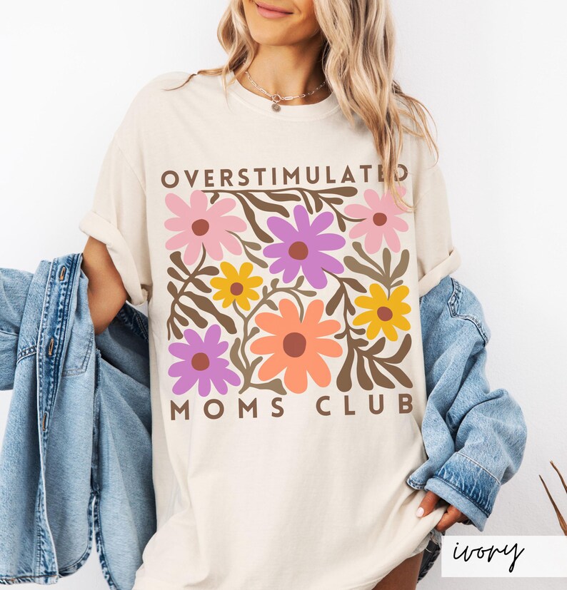 May include: A white t-shirt with a floral design and the text "Overstimulated Moms Club" in brown letters.