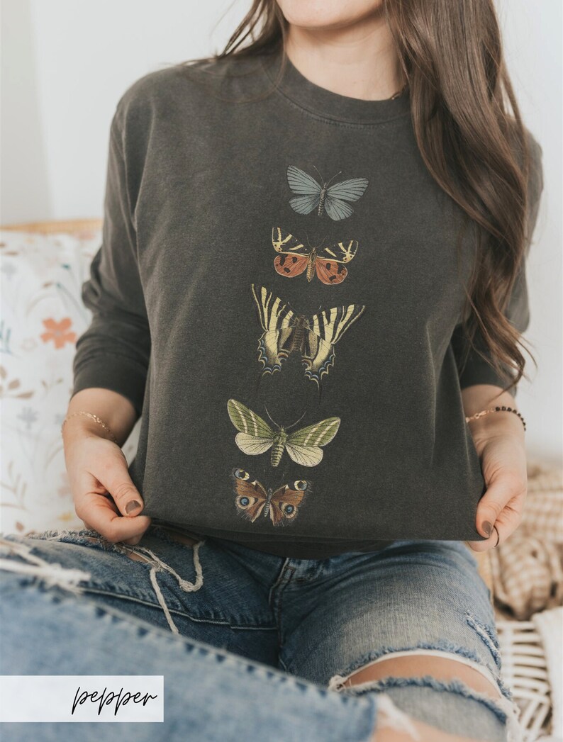 May include: A dark gray sweatshirt with a vertical row of five embroidered butterflies in different colors and patterns. The butterflies are arranged from top to bottom in a descending order of size.