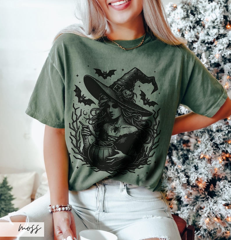 May include: A green t-shirt with a black and white illustration of a witch stirring a cauldron. The witch is wearing a pointed hat and has long, flowing hair. Bats and stars are in the background.