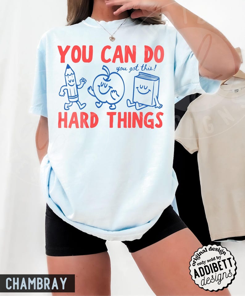 K&ouml;nnte beinhalten: Hellblaues T-Shirt mit rotem Text "YOU CAN DO HARD THINGS" und dem blauen Satz "you got this!". Das Shirt zeigt Cartoon-Illustrationen eines Bleistifts, Apfels und Buches. Original-Design, verkauft von Addibett Designs.
