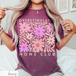 May include: A purple t-shirt with a floral design and the text "Overstimulate Moms Club".