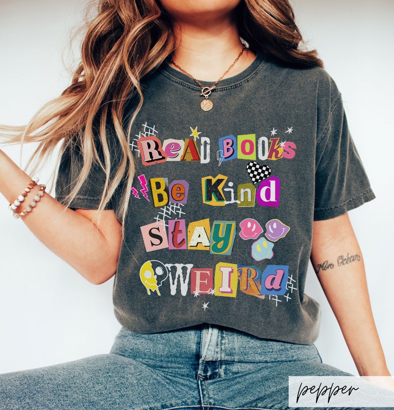 May include: A gray t-shirt with a graphic design that reads "Read Books Be Kind Stay Weird" in colorful, cut-out letters.