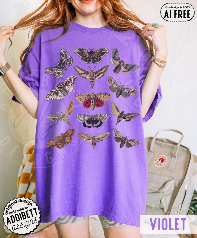 May include: A purple short-sleeve t-shirt featuring a graphic print of twelve different moth species in various shades of brown, gray, and red. The moths are arranged in a grid-like pattern across the front of the garment, showcasing detailed wing markings and textures.