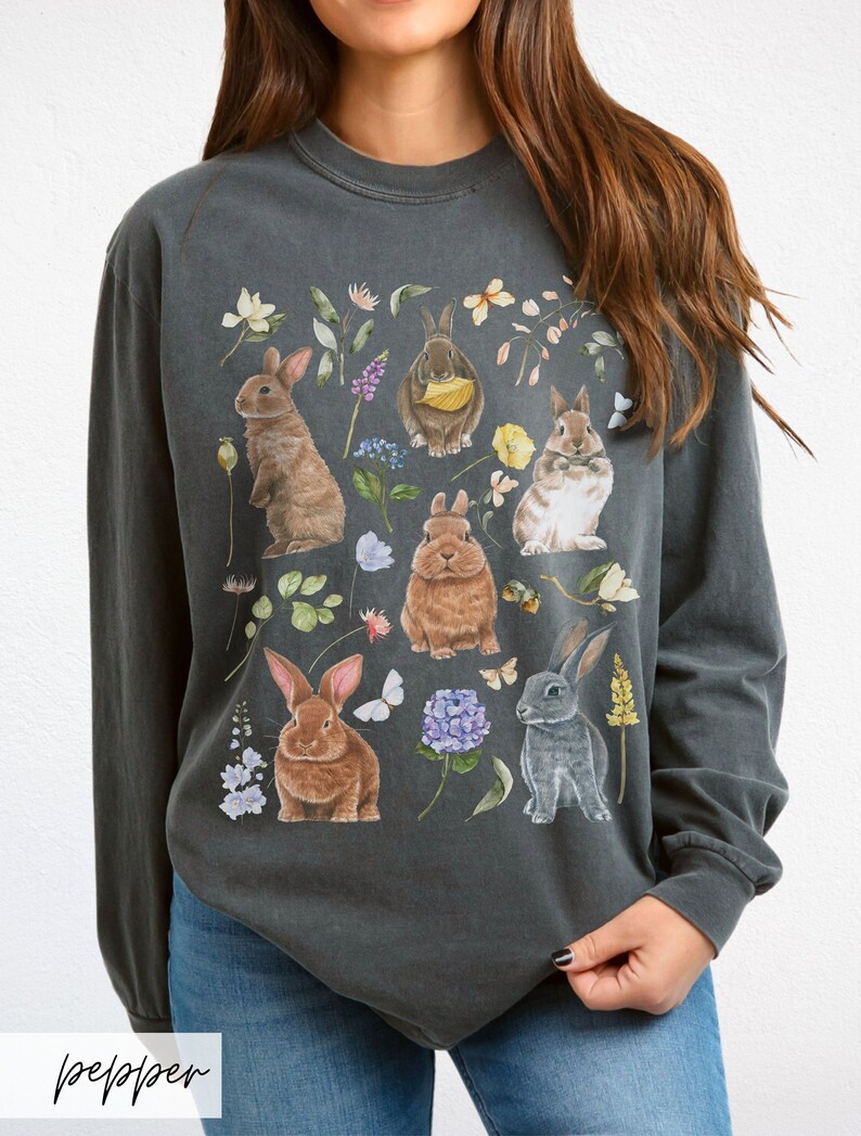 May include: A charcoal grey long-sleeved t-shirt with a graphic print of multiple rabbits and flowers. The rabbits are brown, grey, and white.