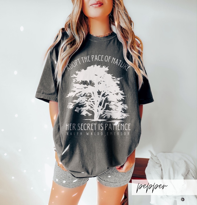 May include: A dark grey t-shirt with a white tree graphic and the text "Adopt the pace of nature. Her secret is patience. Ralph Waldo Emerson".