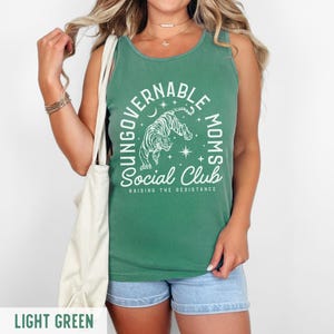 Puede incluir: Camiseta sin mangas verde claro con el texto "YOUNG GOVERNABLE MOMS SOCIAL CLUB RAISING THE RESISTANCE" y un gr&aacute;fico de tigre. La camiseta sin mangas se combina con pantalones cortos de mezclilla azules.