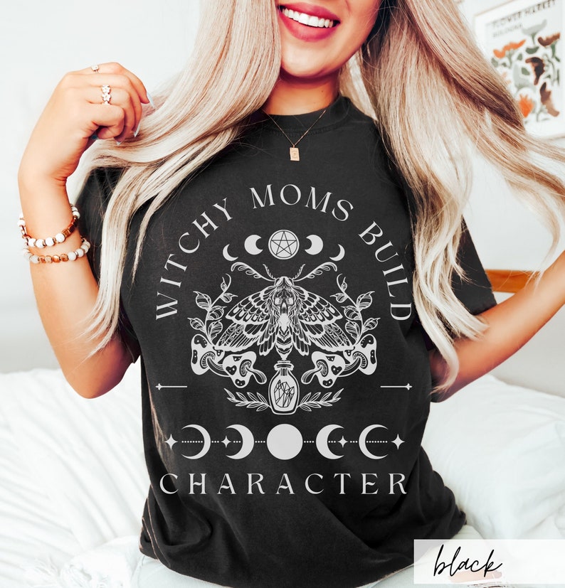 May include: Black t-shirt with a white graphic design featuring a moth, moons, and the text "Witchy Moms Build Character".