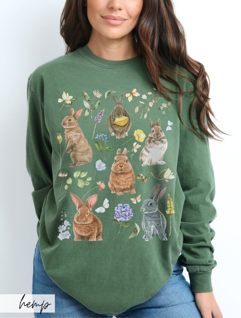 May include: A green long-sleeved sweatshirt with a print of multiple rabbits and flowers. The rabbits are brown and gray and are surrounded by flowers in shades of pink, purple, and yellow.