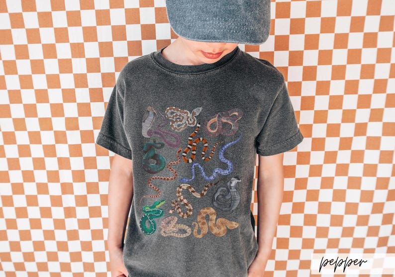 Pode incluir: Uma camiseta cinza escura com uma estampa colorida de v&aacute;rias cobras. As cobras est&atilde;o em diferentes poses e cores, incluindo verde, vermelho, laranja e preto.