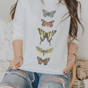 May include: White sweatshirt with a vertical row of five different colored butterflies printed on the front. The butterflies are in various shades of brown, green, yellow, and black.