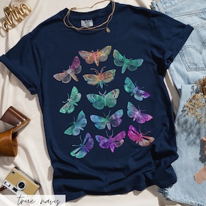 May include: A navy blue t-shirt featuring a colourful print of various butterflies. The butterflies are arranged in a circular pattern and are all different sizes and shapes.