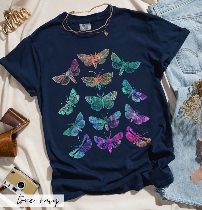 May include: A navy blue t-shirt featuring a colourful print of various butterflies. The butterflies are arranged in a circular pattern and are all different sizes and shapes.