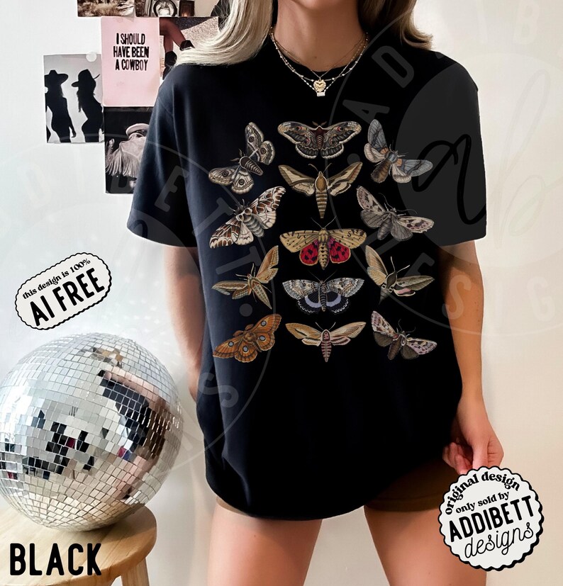May include: A black short-sleeve t-shirt featuring a central graphic print of various moth species in shades of brown, tan, grey, and red. The moths are arranged in a vertical grid pattern across the chest of the shirt, showcasing detailed wing markings.