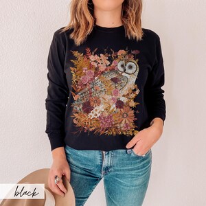 Pode incluir: Camisola preta de manga comprida com uma estampa gr&aacute;fica de uma coruja cercada de flores em tons de marrom, rosa e branco.