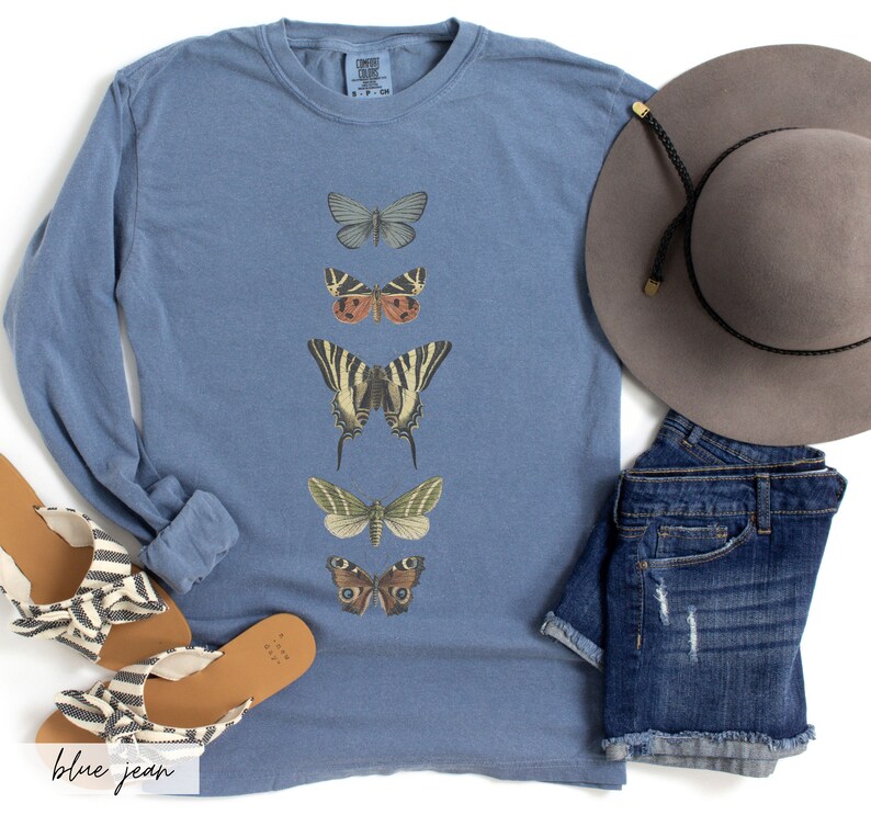 May include: A blue long-sleeve t-shirt with a vertical row of five different butterfly illustrations. The butterflies are in various colors, including brown, green, yellow, black, and white.