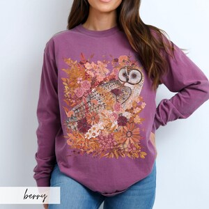 Pode incluir: Uma camisa de manga comprida roxa com uma estampa gr&aacute;fica de uma coruja cercada por flores de outono. A coruja &eacute; marrom e branca com olhos amarelos. As flores s&atilde;o em tons de laranja, amarelo, rosa e vermelho.
