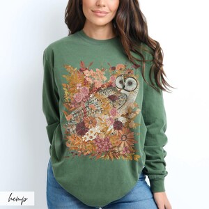 Pode incluir: Uma camisa verde de manga comprida com uma estampa de uma coruja cercada por flores e folhas. A coruja &eacute; marrom e branca com olhos amarelos.