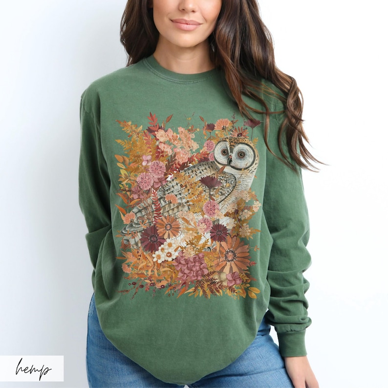 Pode incluir: Uma camisa verde de manga comprida com uma estampa de uma coruja cercada por flores e folhas. A coruja &eacute; marrom e branca com olhos amarelos.