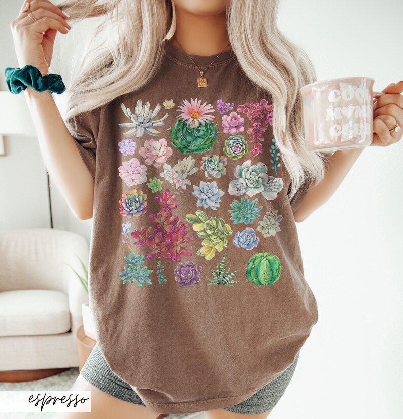 Puede incluir: Una camiseta marr&oacute;n de gran tama&ntilde;o con un estampado de suculentas de colores. La camiseta tiene un corte holgado y cuello redondo.