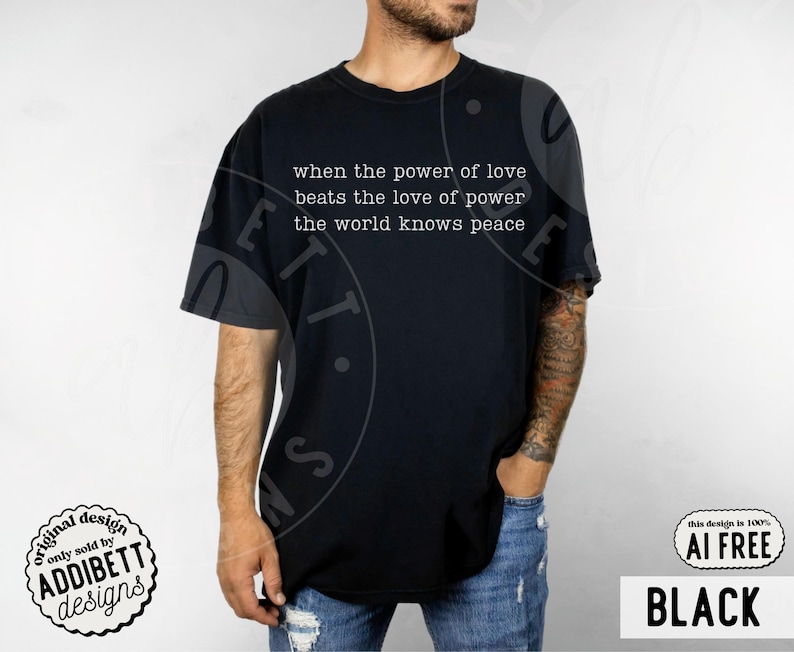 May include: A black short-sleeved t-shirt featuring white text printed on the chest that reads: when the power of love beats the love of power the world knows peace. The shirt has a crew neckline and a standard fit, shown in a solid black color.