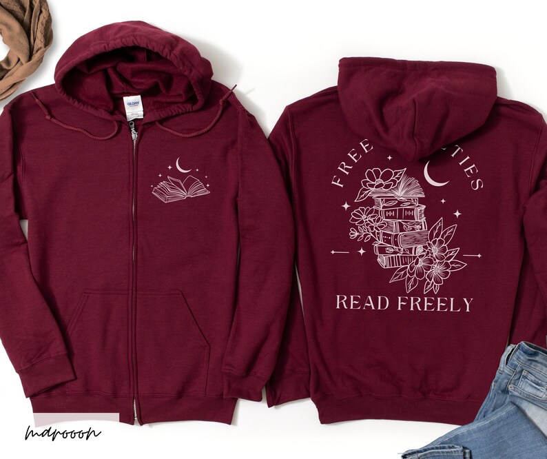 May include: Maroon zip-up hoodie with a white graphic of an open book, moon, and stars on the front. The back features a stack of books, flowers, a crescent moon, and the words "FREE" and "READ FREELY".
