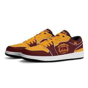 Puede incluir: Zapatillas bajas en color burdeos y dorado con cordones amarillos. El lateral presenta un gráfico de un balón de fútbol americano con el horizonte de una ciudad y el texto WASHINGTON, con un pequeño icono de bandera de tres estrellas encima.