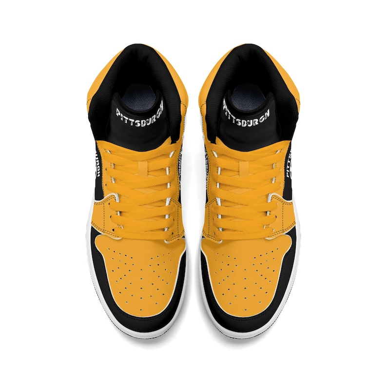 Peut inclure: Paire de baskets montantes, vue de dessus. Les chaussures ont un col et une languette noirs avec le mot "PITTSBURGH" imprim&eacute; sur la languette. Le corps de la chaussure est jaune avec des accents noirs et une semelle blanche.
