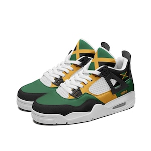 May include: A pair of athletic sneakers featuring a color scheme of green, yellow, and black, inspired by the Jamaican flag. The shoes have white laces, white mesh side panels, black structural eyelet wings, and the word YAADIE printed on the side.
