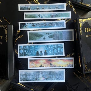 May include: A collection of Harry Potter book-themed items. The image shows several black books with gold lettering and illustrations, along with rectangular bookmarks featuring scenes from the books. The bookmarks depict various scenes in watercolor.
