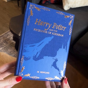 May include: A blue hardcover book titled "Harry Potter and the Prisoner of Azkaban" with gold lettering and decorative accents. The cover features a silhouette design. The author's name, J.K. Rowling, is printed at the bottom.