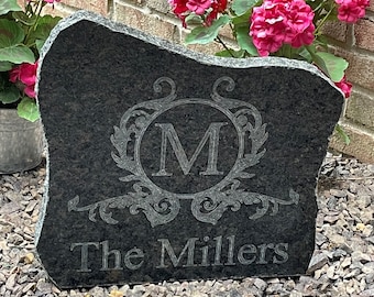 May include: A black granite stone with a decorative engraved design featuring the letter "M" in a circle surrounded by a floral pattern. The text "The Millers" is engraved below the design.