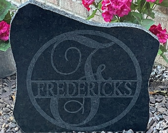 May include: Black granite stone with a carved monogram of the letter "F" and the name "FREDERICKS" in a circle.