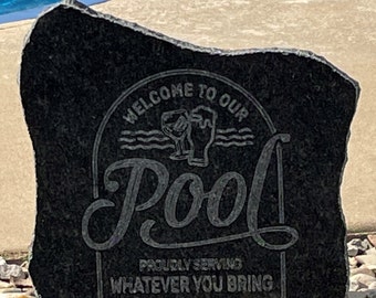 May include: Black granite rock with a white inscription that reads "Welcome to our Pool, Proudly Serving Whatever You Bring". The inscription is in a circle with a stylized image of a glass and a beer mug.