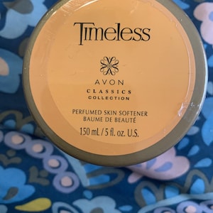 Peut inclure: Un récipient rond brun clair de l'adoucissant pour la peau parfumé Timeless de la collection Avon Classics. L'étiquette indique "150 ml". Le récipient est enveloppé dans du plastique transparent.
