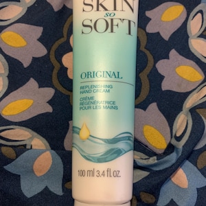 Może przedstawiać: Tubka kremu do rąk Avon Skin So Soft Original. Tubka jest biało-turkusowa z nazwą marki i szczegółami produktu. Zawiera 100 ml kremu.
