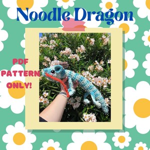 Op de afbeelding: Een gehaakte Noodle Dragon in blauw en wit, met een rode tong, gehouden tegen een achtergrond van bloemen. De afbeelding bevat de tekst "Noodle Dragon" en "PDF PATTERN ONLY!"