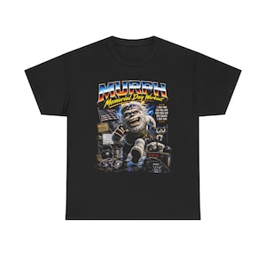 May include: Black t-shirt with a graphic featuring a cartoon yeti running. The text reads "MURPH Memorial Day Workout" in a retro font. The design includes an American flag and workout details.