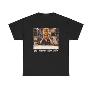 May include: Black t-shirt featuring a graphic of a doll dressed as a nurse in a hospital setting. The doll is surrounded by medical equipment and the text "yay. another night shift." is printed below the image.