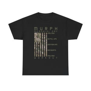 Peut inclure: T-shirt noir avec l'inscription "MURPH MEMORIAL DAY WORKOUT" dans une police de style militaire. Le motif comprend un drapeau américain avec un motif camouflage et des instructions d'entraînement : 1 mile de course, 100 tractions, 200 pompes, 300 squats et 1 mile de course.