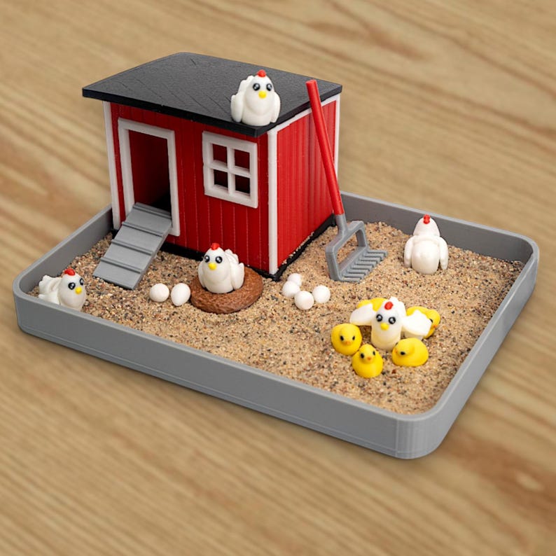 Puede incluir: Un gallinero en miniatura rojo y blanco con techo negro se asienta en una bandeja gris llena de arena. El conjunto incluye varias figuras de gallinas blancas, pollitos amarillos, huevos blancos, un nido marr&oacute;n y un rastrillo rojo.
