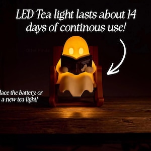 Front view of a glowing reading ghost in its chair. Text states: LED Tea light lasts about 14 days of continuous use! Easily replace the battery or swap in a new tea light!