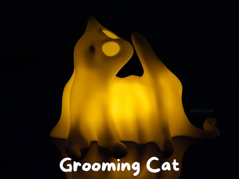 Pode incluir: Uma l&acirc;mpada amarela brilhante em forma de gato numa pose de limpeza contra um fundo preto. A l&acirc;mpada emite uma luz quente, destacando a silhueta felina e o texto Grooming Cat na parte inferior. O design apresenta bordas suaves e arredondadas.