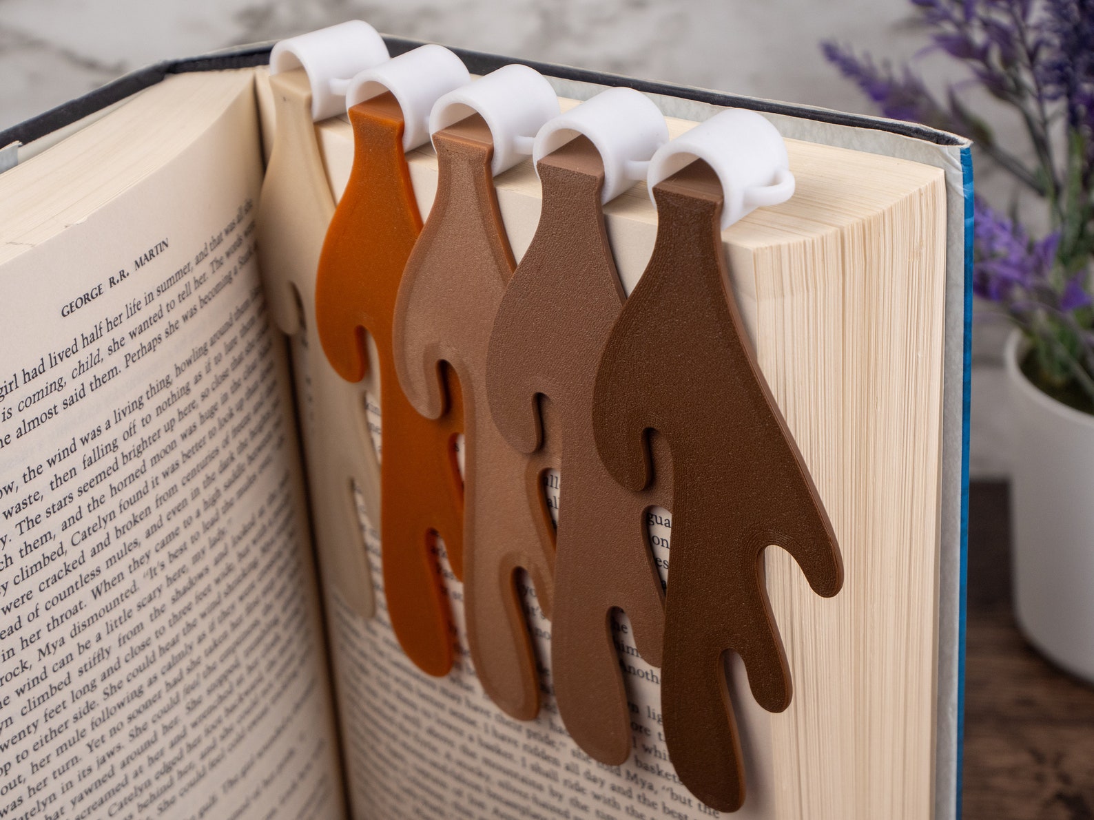 An open book with five felt bookmarks of different colors that look like spilled coffee.